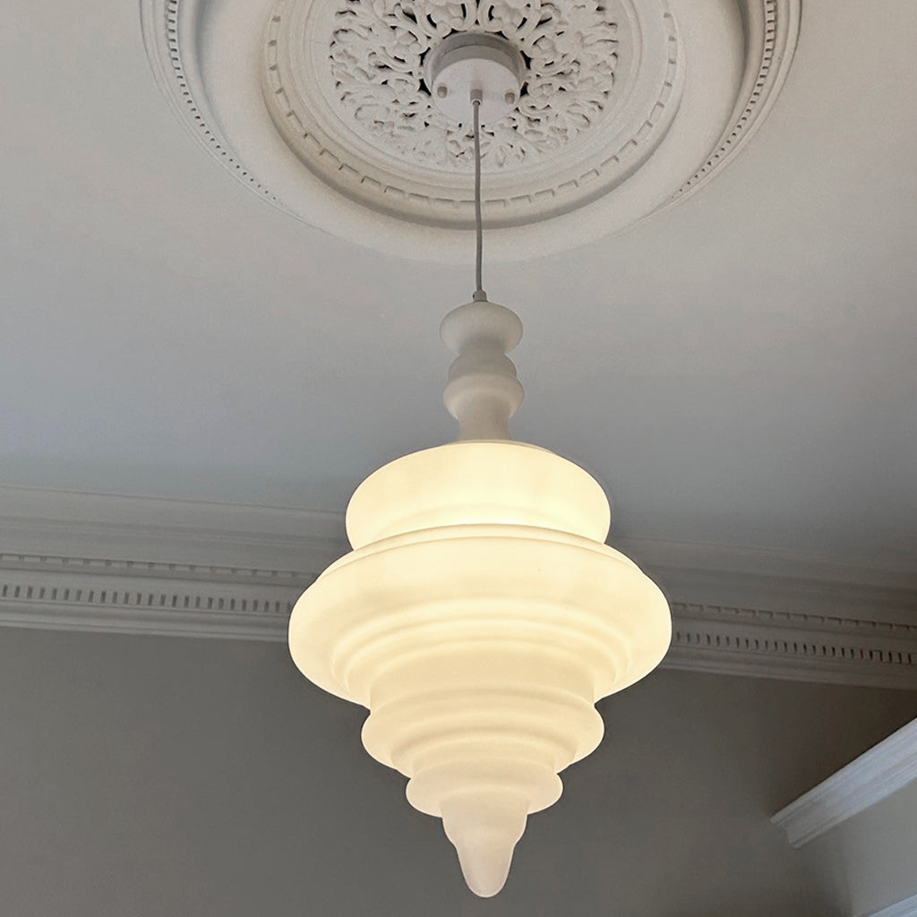 A white, sculptural pendant light with a tiered design hanging in a villa bedroom.