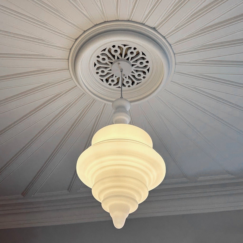 A white, sculptural pendant light with a tiered design hanging in a villa bedroom.
