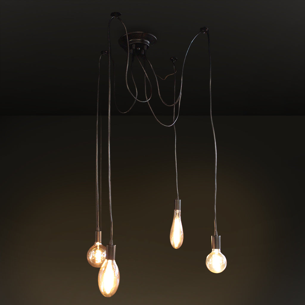 A multi-light pendant chandelier with a dark metal ceiling canopy and four thin hanging cords, each ending in a glowing exposed bulb, shown against a dark wall and ceiling.