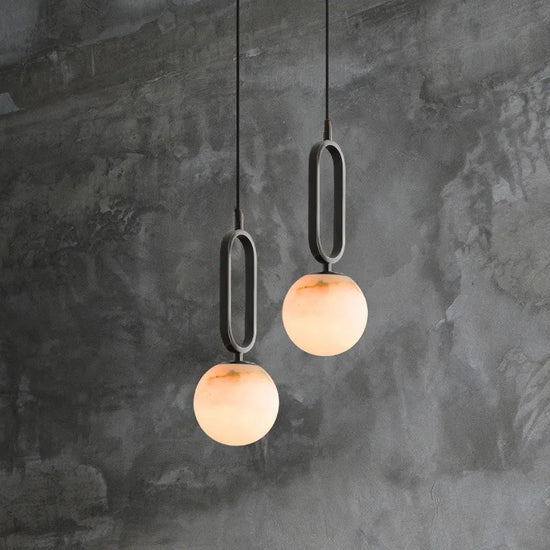 Two Zara pendant lights with a matt black frame and real Alabaster stone diffuser, hanging against a textured grey wall.