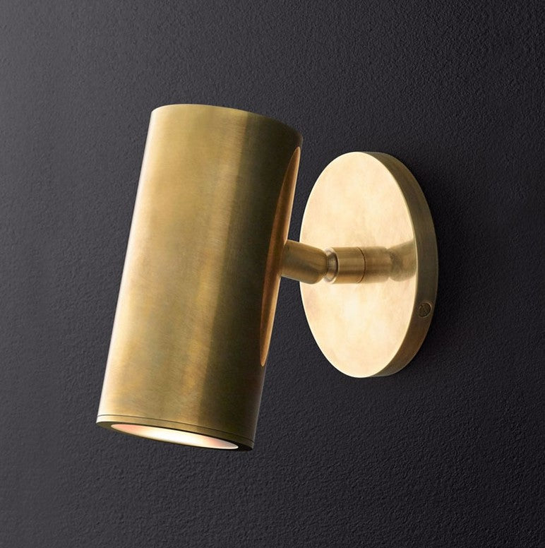 A cylindrical brushed brass wall light fixture mounted on a wall.