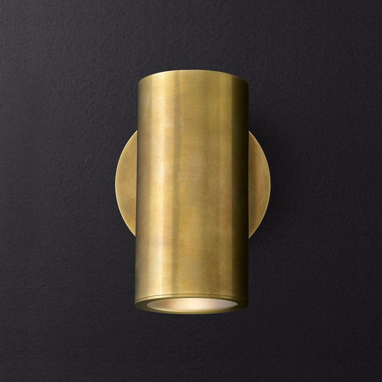 A cylindrical brushed brass wall light fixture mounted on a wall.