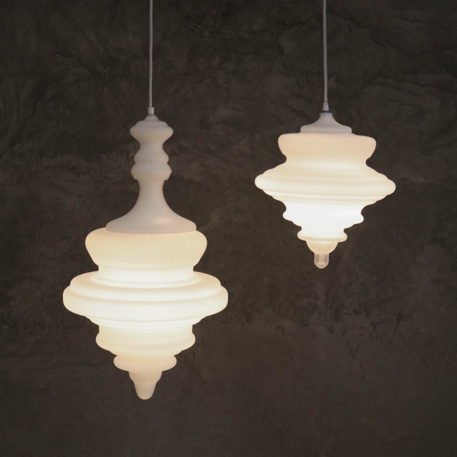 Two white glass pendant lights with a opaque white finish, hanging against a dark background.