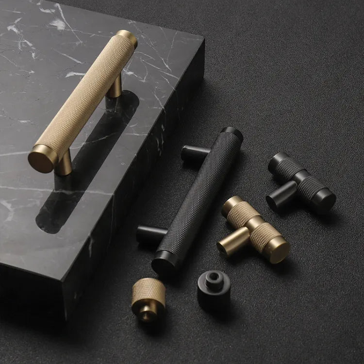 A gold-colored brass handle lying on a flat surface with a plain background.